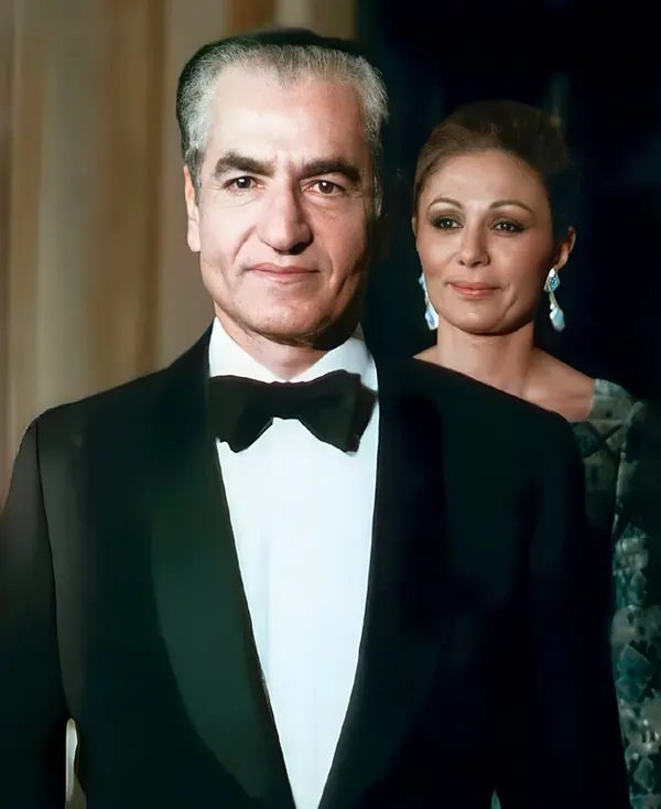 His Majesty, the Shah of Iran in a tuxedo and bow tie stands before Farah Pahlavi, Empress of Iran, wearing elegant earrings — a public domain photograph from The Shah of Iran archive documenting the Pahlavi era.