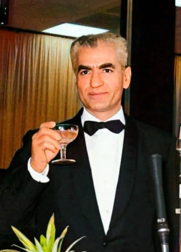His Majesty, the Shah of Iran in a tuxedo and bow tie holds a glass of liquid in his hand — a public domain photograph from The Shah of Iran archive documenting the Pahlavi era.