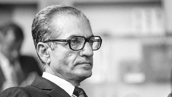 His Majesty, the Shah of Iran wearing glasses and a dark suit looks off-camera in a close-up portrait — a public domain photograph from The Shah of Iran archive documenting the Pahlavi era.