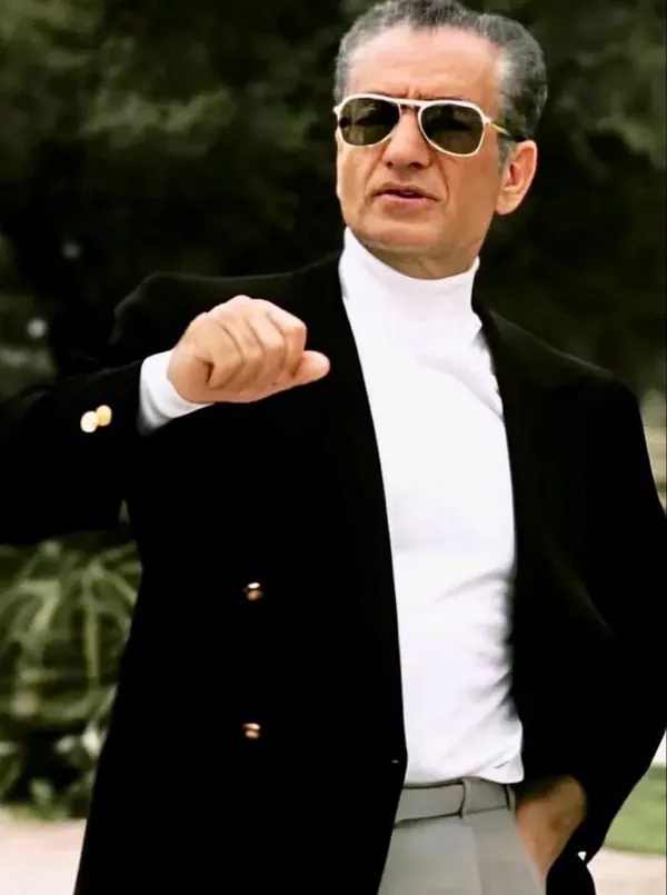 His Majesty, the Shah of Iran wearing sunglasses, a white turtleneck, and a black blazer gestures with one hand — a public domain photograph from The Shah of Iran archive documenting the Pahlavi era.