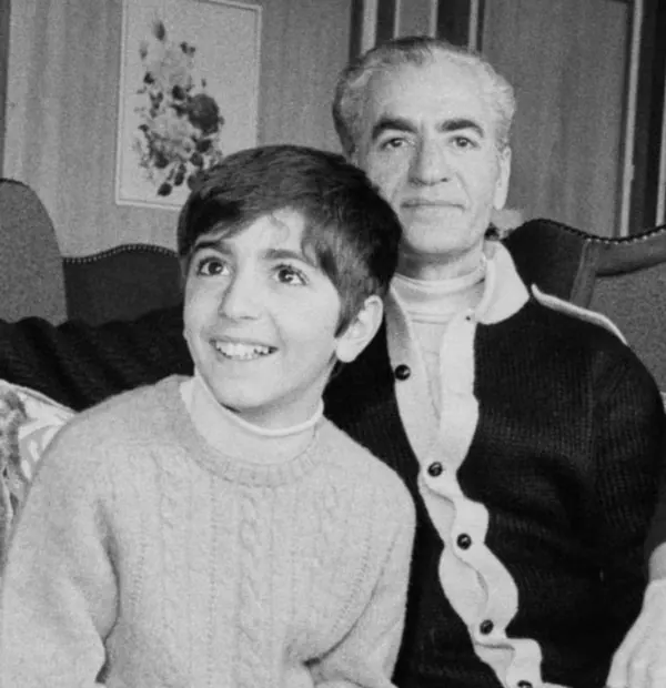 An older man in a dark cardigan sits beside a young boy wearing a light-colored sweater — a public domain photograph from The Shah of Iran archive documenting the Pahlavi era.