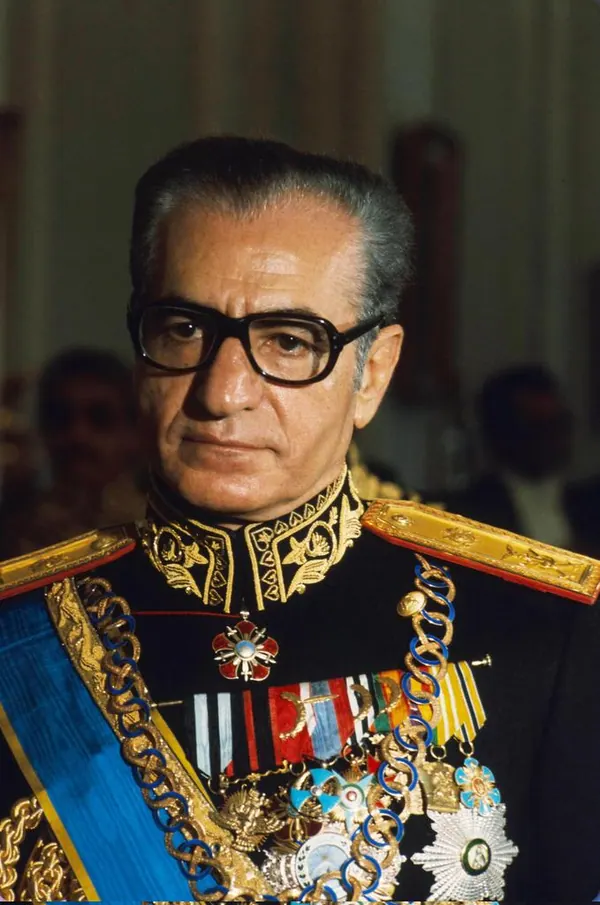 An older man in a dark military uniform with gold embroidery and numerous medals looks forward — a public domain photograph from The Shah of Iran archive documenting the Pahlavi era.