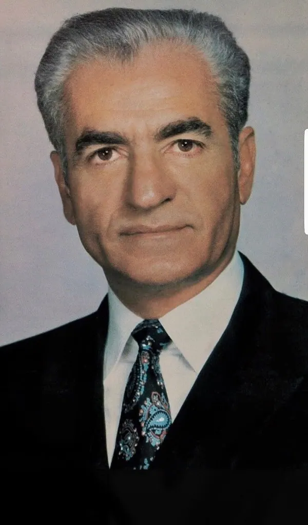 An older man with grey hair wears a dark suit, white shirt, and patterned tie in a portrait — a public domain photograph from The Shah of Iran archive documenting the Pahlavi era.