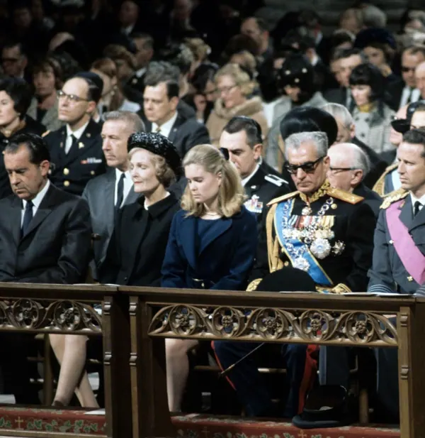 People in formal attire and military uniforms sit in rows of ornate wooden pews during a gathering — a public domain photograph from The Shah of Iran archive documenting the Pahlavi era.