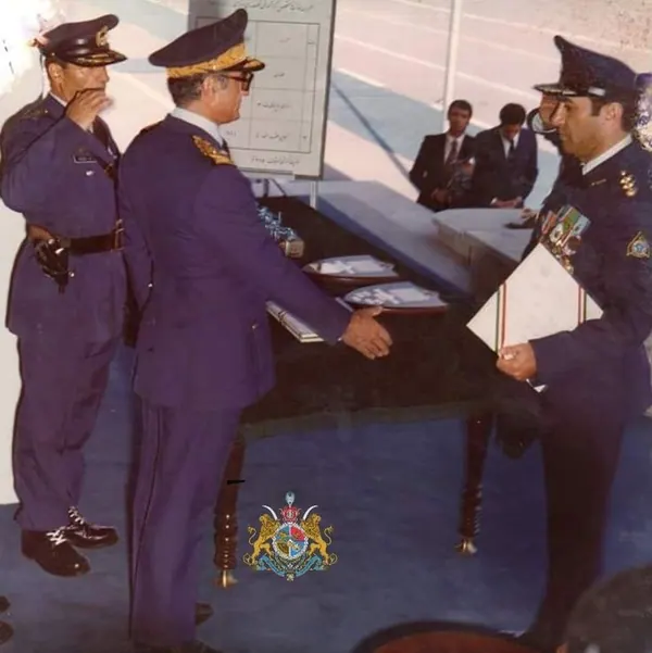 His Majesty, the Shah of Iran, and others in blue military uniforms stand in a room, with one handing a document to another — a public domain photograph from The Shah of Iran archive documenting the Pahlavi era.