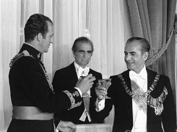 His Majesty, the Shah of Iran, and others in formal attire and uniforms hold glasses of liquid while standing in a room with curtains — a public domain photograph from The Shah of Iran archive documenting the Pahlavi era.
