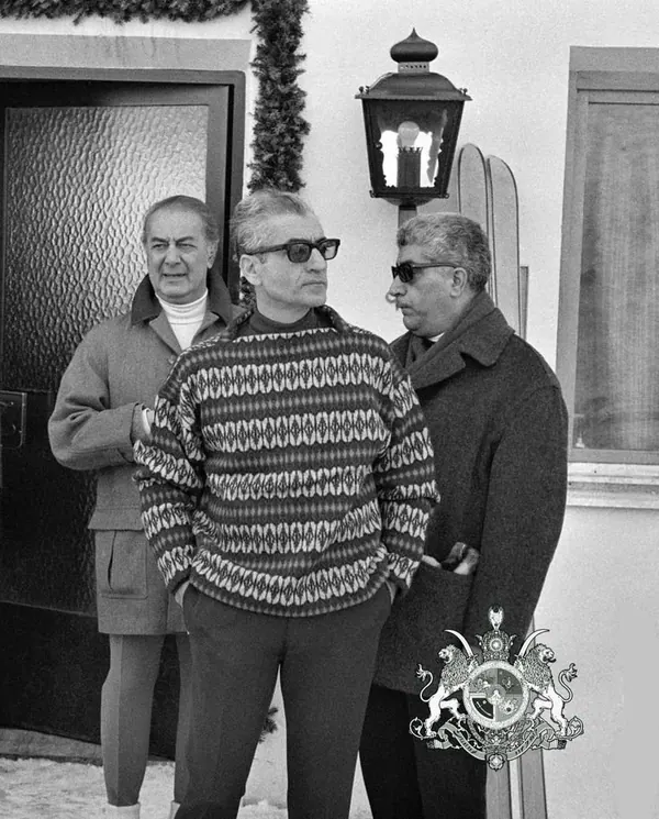 His Majesty, the Shah of Iran, and others in winter clothing stand outdoors near a doorway and a lamp post — a public domain photograph from The Shah of Iran archive documenting the Pahlavi era.