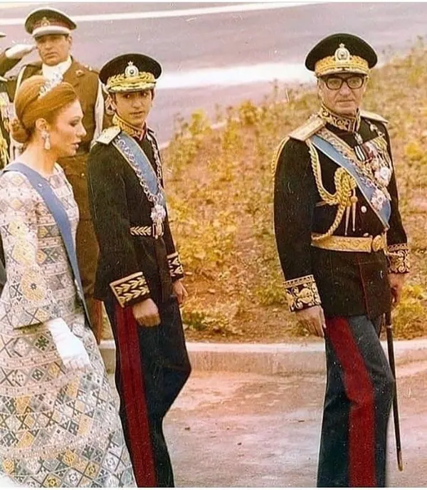 Three people in formal attire and military uniforms stand outdoors against a background of greenery — a public domain photograph from The Shah of Iran archive documenting the Pahlavi era.