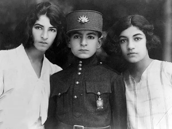 Three young people pose for a portrait, with a youth in military uniform between two girls — a public domain photograph from The Shah of Iran archive documenting the Pahlavi era.