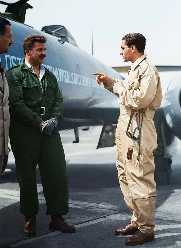 His Majesty, the Shah of Iran, and others in flight suits stand on a tarmac talking in front of a large jet aircraft — a public domain photograph from The Shah of Iran archive documenting the Pahlavi era.
