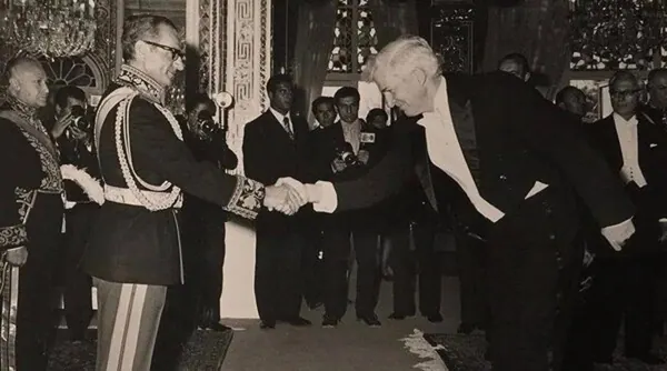 His Majesty, the Shah of Iran, and others in formal attire shake hands in a room while other men in suits look on — a public domain photograph from The Shah of Iran archive documenting the Pahlavi era.
