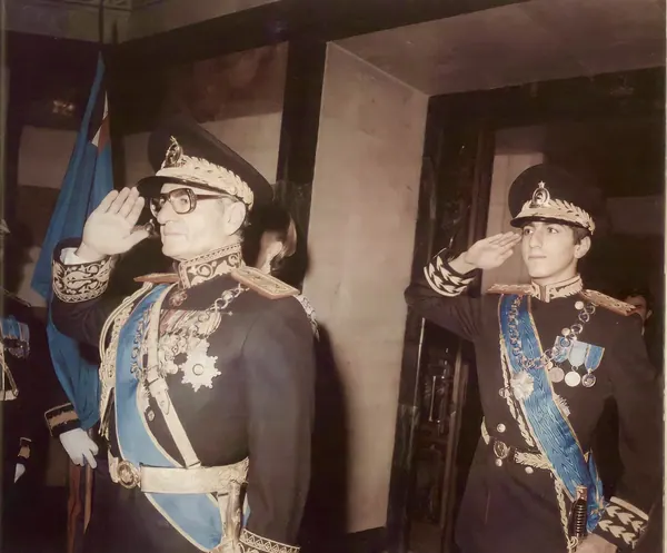 His Majesty, the Shah of Iran, and others in ornate dark military uniforms with sashes and medals stand saluting indoors — a public domain photograph from The Shah of Iran archive documenting the Pahlavi era.