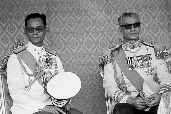 His Majesty, the Shah of Iran, and others in ornate white military uniforms and sunglasses sit side by side against a patterned wall — a public domain photograph from The Shah of Iran archive documenting the Pahlavi era.