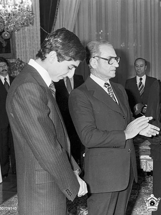 His Majesty, the Shah of Iran, and others in suits stand indoors near a chandelier, with one man gesturing with his hands — a public domain photograph from The Shah of Iran archive documenting the Pahlavi era.