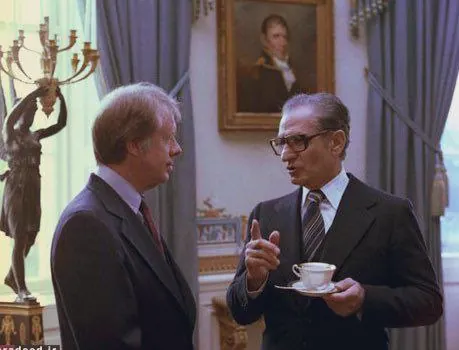 Two middle-aged men in dark suits talk in a room with a painting and a candelabra — a public domain photograph from The Shah of Iran archive documenting the Pahlavi era.