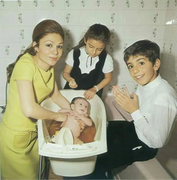 Farah Pahlavi, Empress of Iran, a girl, and a boy gather around a baby in a white plastic bathtub — a public domain photograph from The Shah of Iran archive documenting the Pahlavi era.