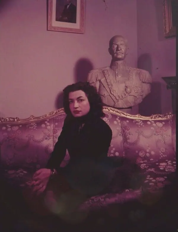 Farah Pahlavi, Empress of Iran, in a dark dress sits on an ornate sofa in front of a military bust — a public domain photograph from The Shah of Iran archive documenting the Pahlavi era.