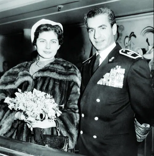 Farah Pahlavi, Empress of Iran, in a fur coat and hat holds flowers beside His Majesty in a decorated military uniform — a public domain photograph from The Shah of Iran archive documenting the Pahlavi era.