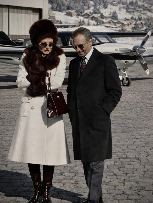 Farah Pahlavi, Empress of Iran, in a white coat and fur hat walks beside His Majesty in a dark overcoat near a plane — a public domain photograph from The Shah of Iran archive documenting the Pahlavi era.