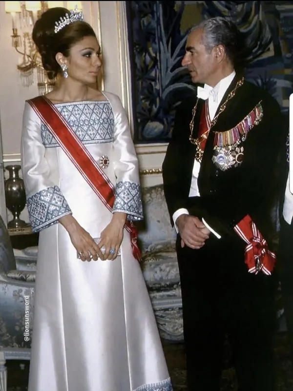 Farah Pahlavi, Empress of Iran, in a white gown and tiara stands beside His Majesty in a formal black uniform — a public domain photograph from The Shah of Iran archive documenting the Pahlavi era.