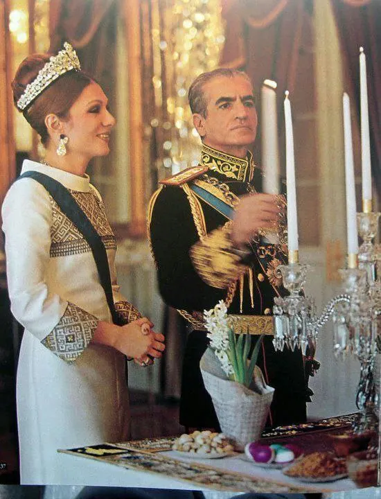 Farah Pahlavi, Empress of Iran, in a white gown and tiara stands beside His Majesty in a dark military uniform — a public domain photograph from The Shah of Iran archive documenting the Pahlavi era.