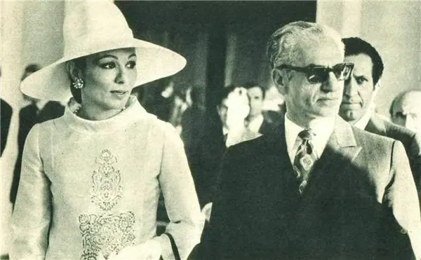 Farah Pahlavi, Empress of Iran, in a wide-brimmed hat and light dress stands beside His Majesty wearing sunglasses and a suit — a public domain photograph from The Shah of Iran archive documenting the Pahlavi era.